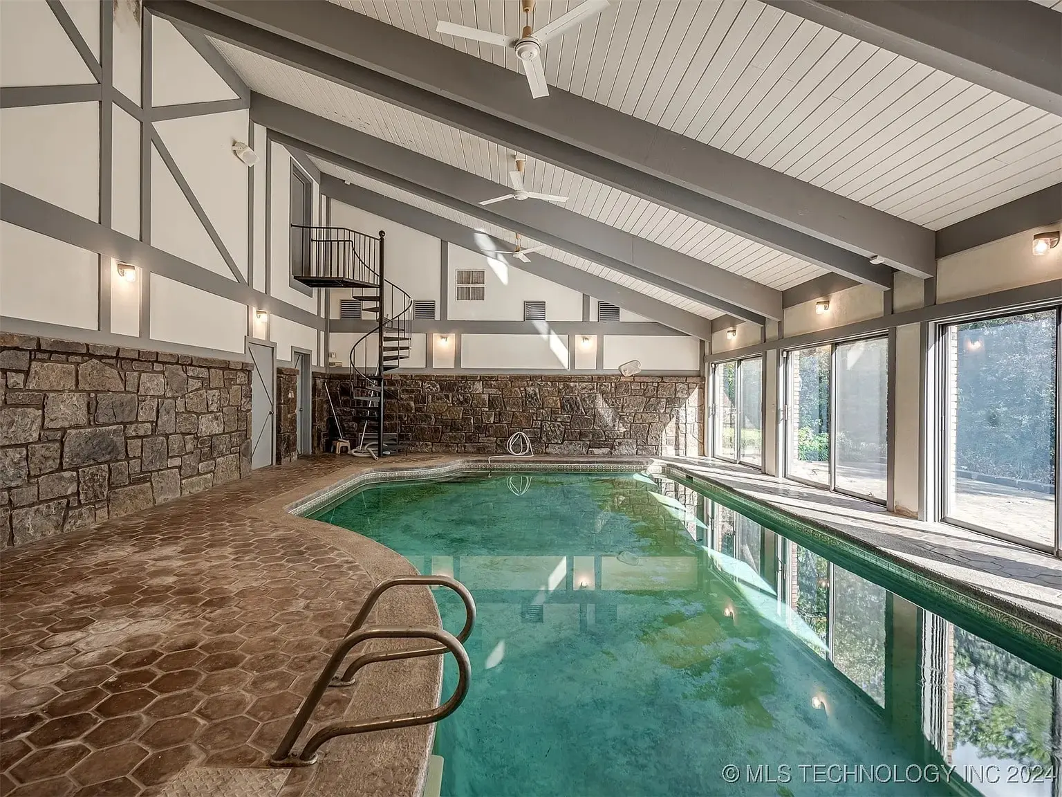 Indoor swimming pool with stone walls, large windows, and a spiral staircase.