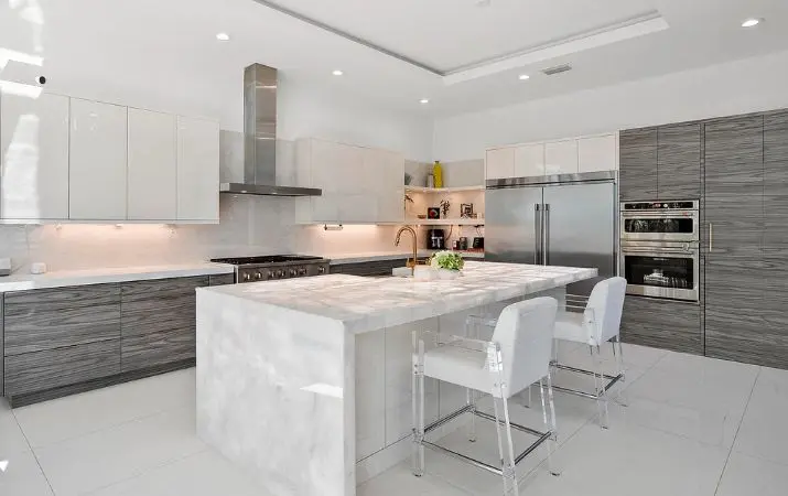 Modern kitchen with marble island, stainless steel appliances, white cabinets, and two bar stools.