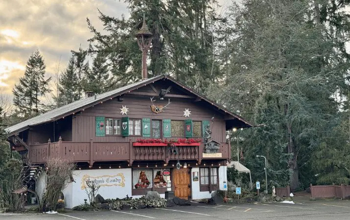 Alpine-style building with Christmas decorations, surrounded by tall trees, and a sign reading 'Olympic Candy'.