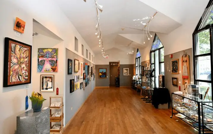 Art gallery hallway with colorful paintings on walls, wooden floor, and display cases on the right.