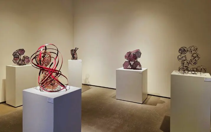 Art gallery with five abstract wire sculptures on white pedestals in a well-lit room.