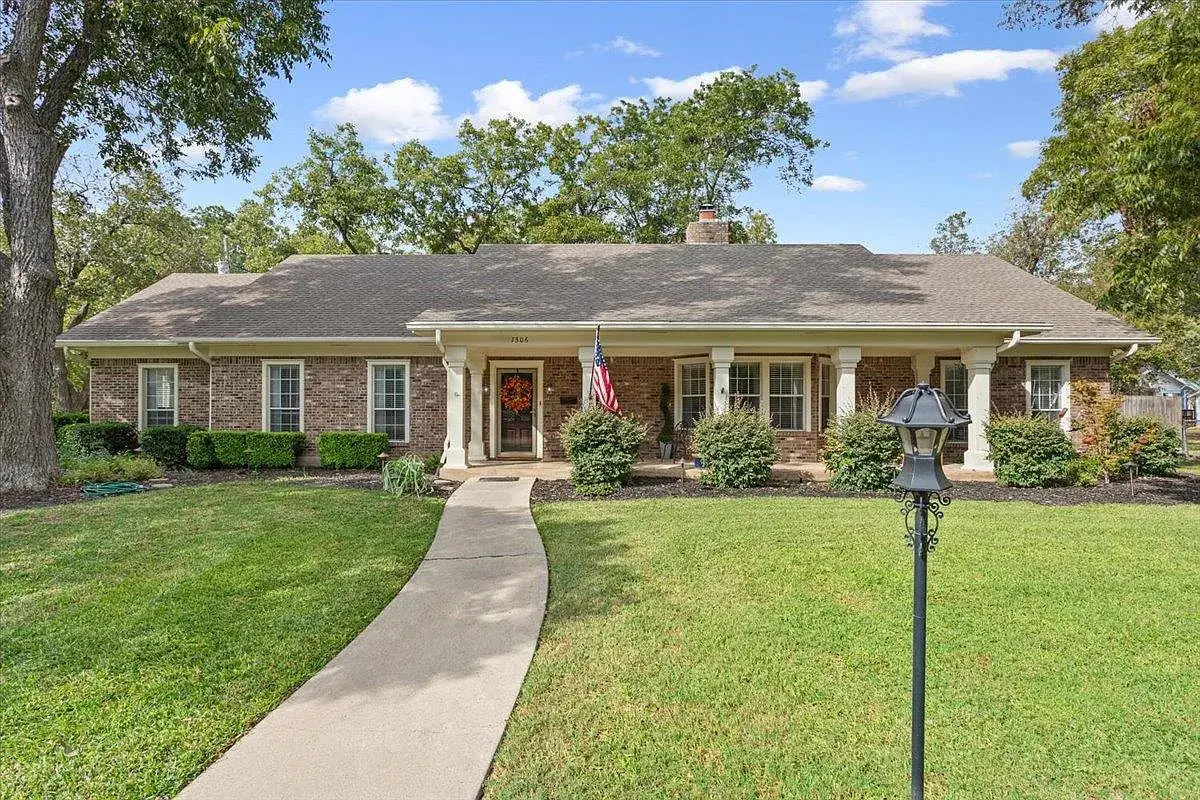 Single-story brick house with a front porch, American flag, and a well-maintained lawn.