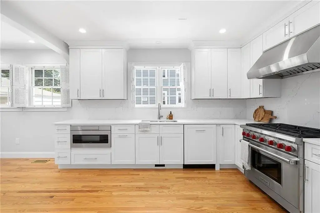 Modern kitchen with white cabinets, stainless steel appliances, and hardwood floors. Bright natural lighting.