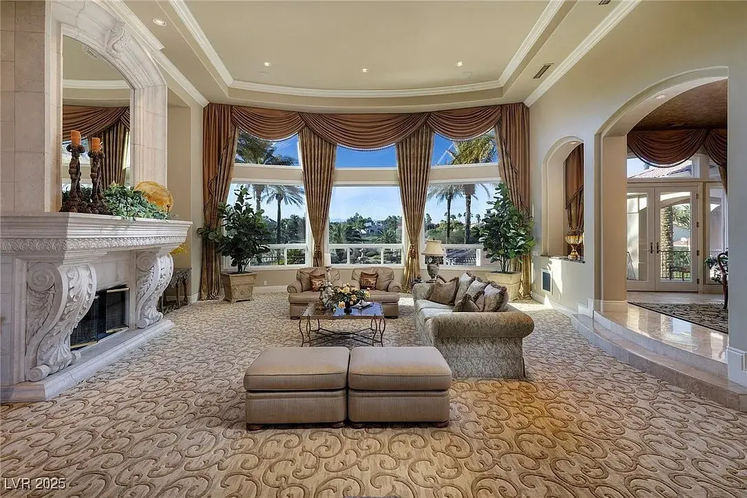Luxurious living room with large windows, elegant furniture, ornate fireplace, and lush outdoor view.
