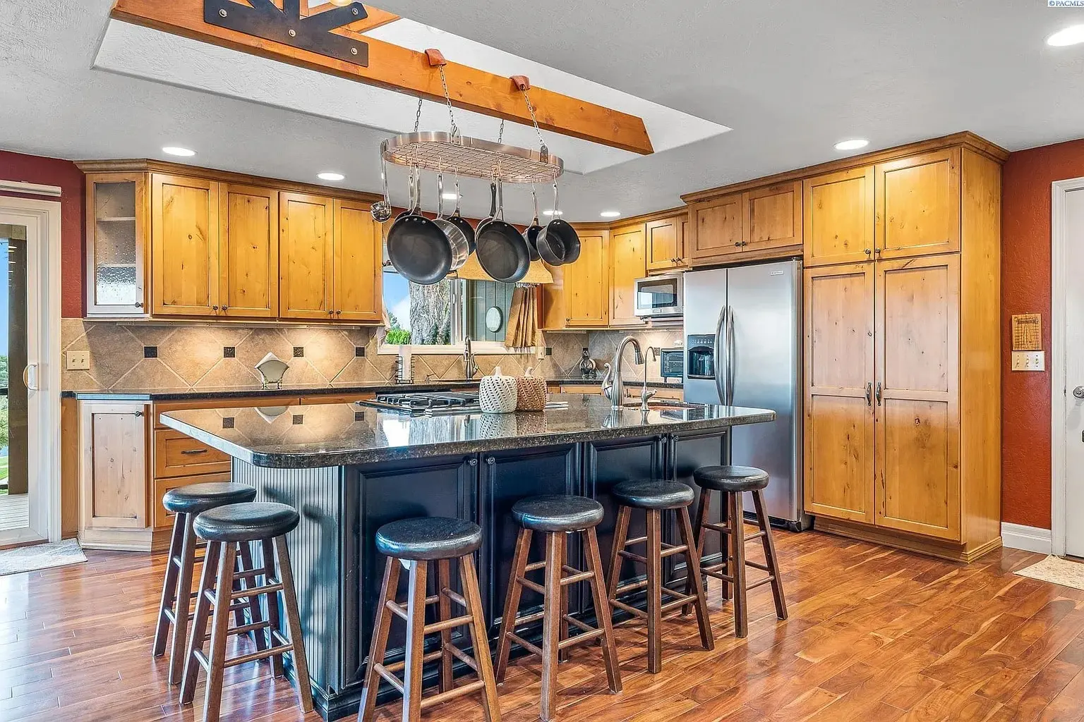 Spacious kitchen with wooden cabinets, large island, hanging pots, and stainless steel appliances.