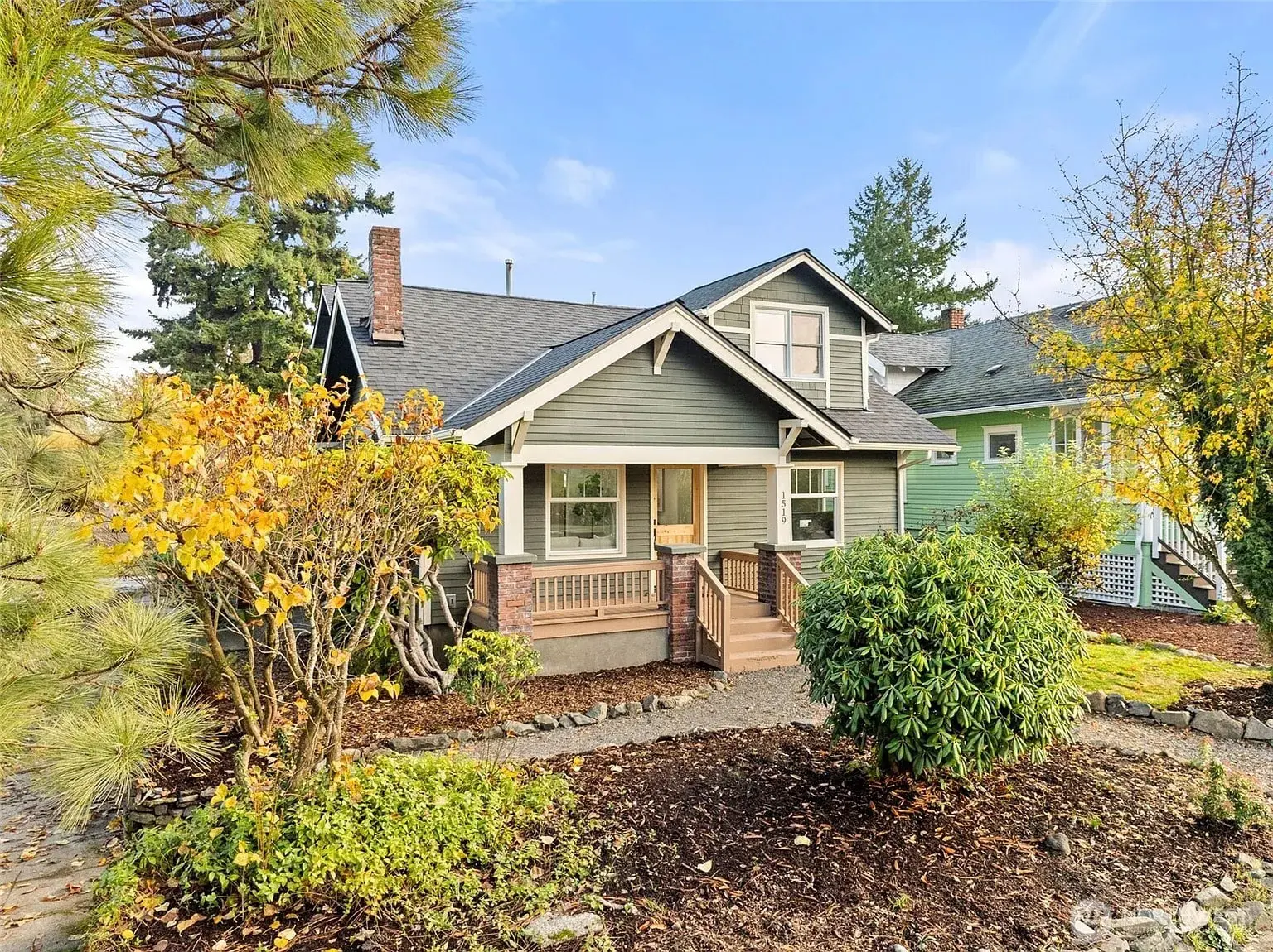 A charming gray house with a porch, surrounded by trees and shrubs, under a clear sky.