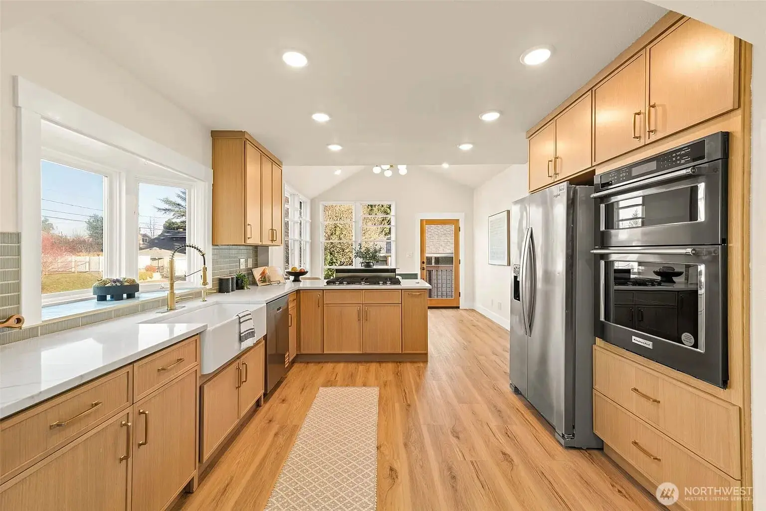 Modern kitchen with wooden cabinets, stainless steel appliances, and large windows providing natural light.