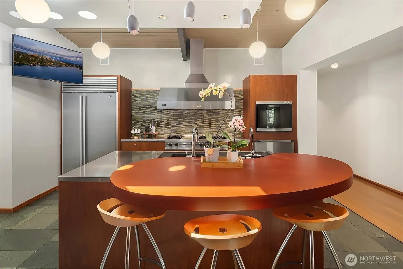 Modern kitchen with round island, bar stools, stainless steel appliances, and pendant lighting.