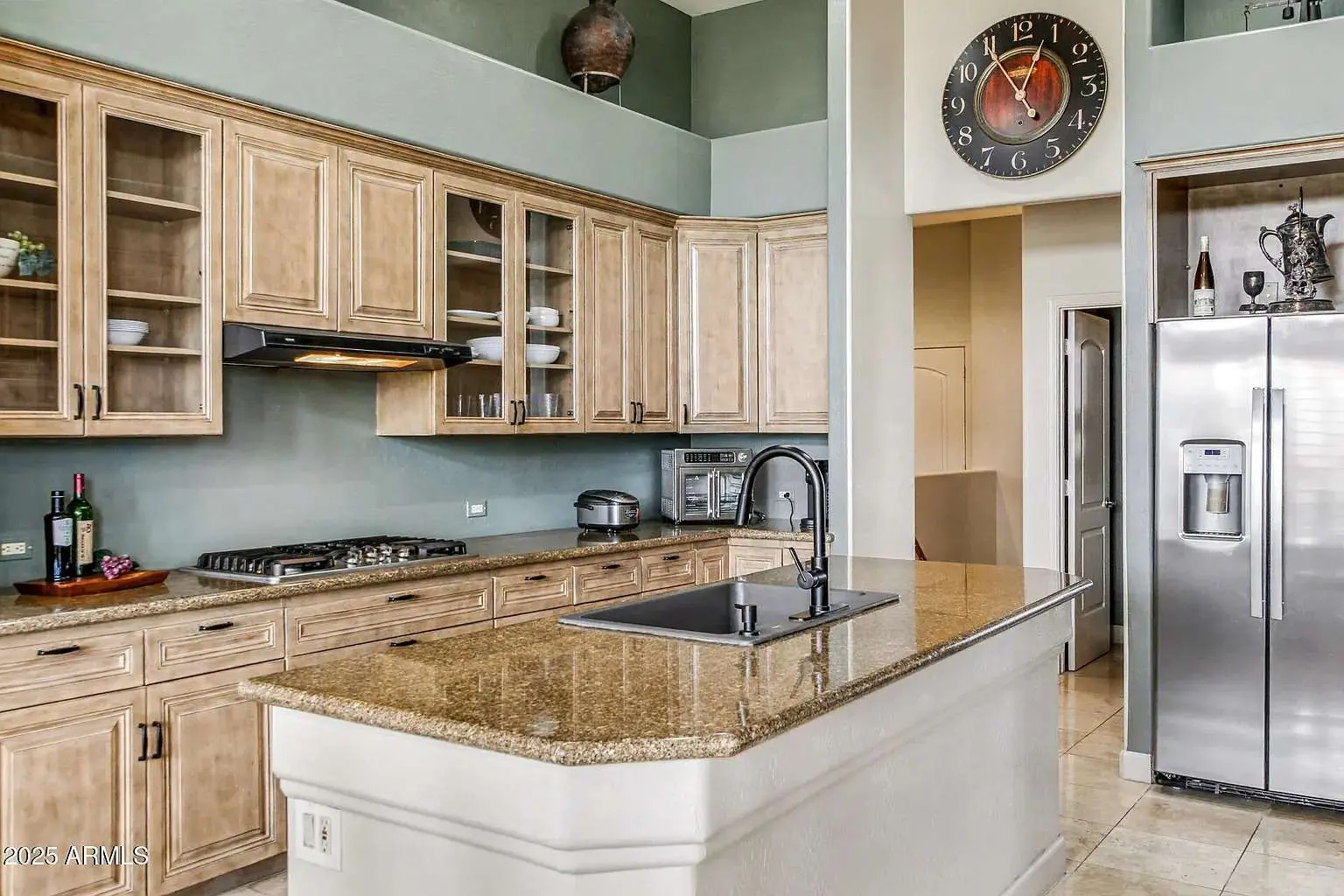 Modern kitchen with wooden cabinets, granite countertops, stainless steel appliances, and a large wall clock.