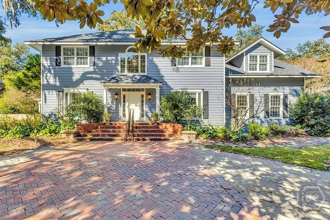 Two-story blue house with white trim, brick steps, and a herringbone brick driveway.