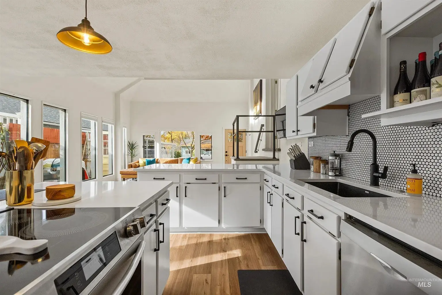 Modern kitchen with white cabinets, black hardware, and a view into a bright living area.