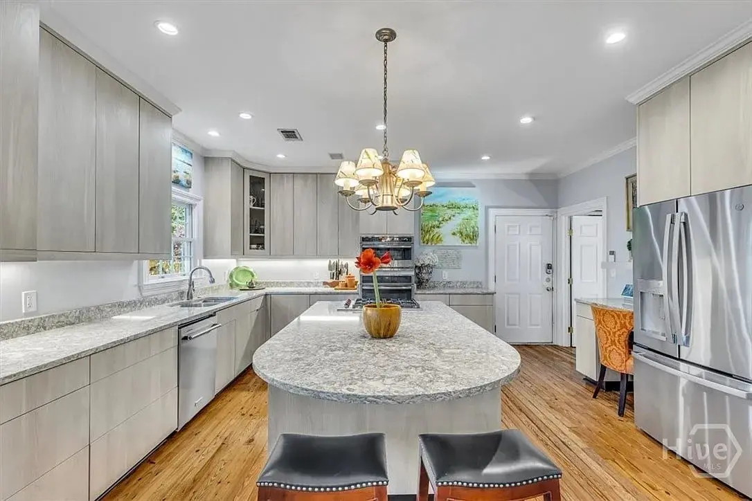 Modern kitchen with large island, stainless steel appliances, wooden floor, and decorative chandelier.