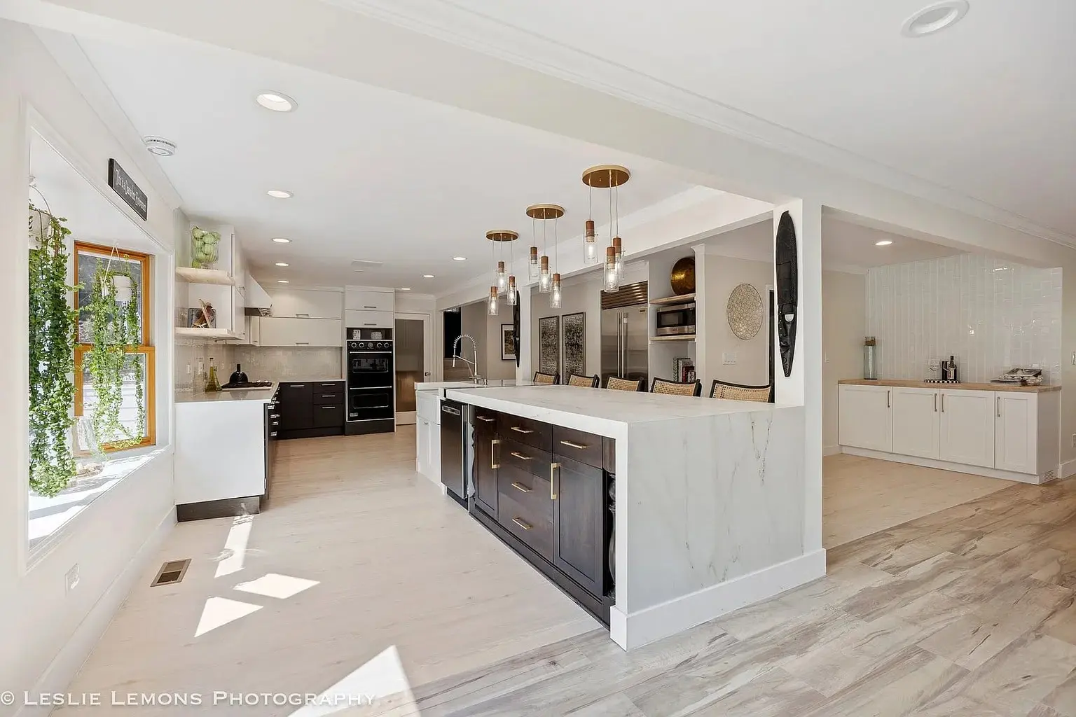 Modern kitchen with large island, pendant lights, white cabinets, and wooden flooring. Bright and spacious.