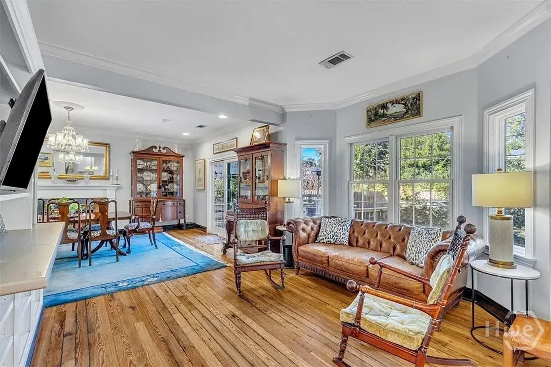 Spacious living room with vintage furniture, wooden floor, and large windows overlooking greenery.