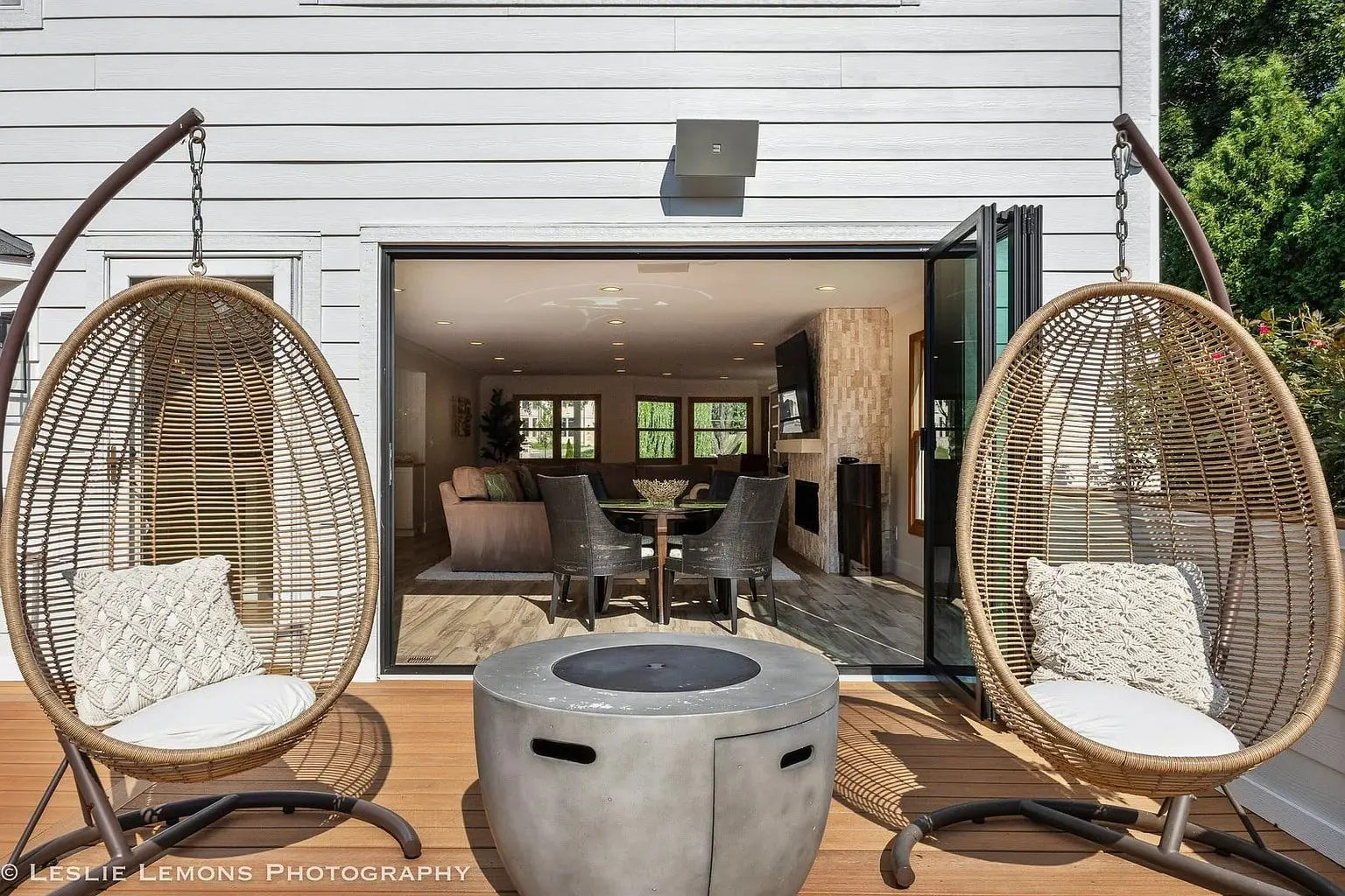 Outdoor patio with two hanging egg chairs, a fire pit, and open doors to a living room.