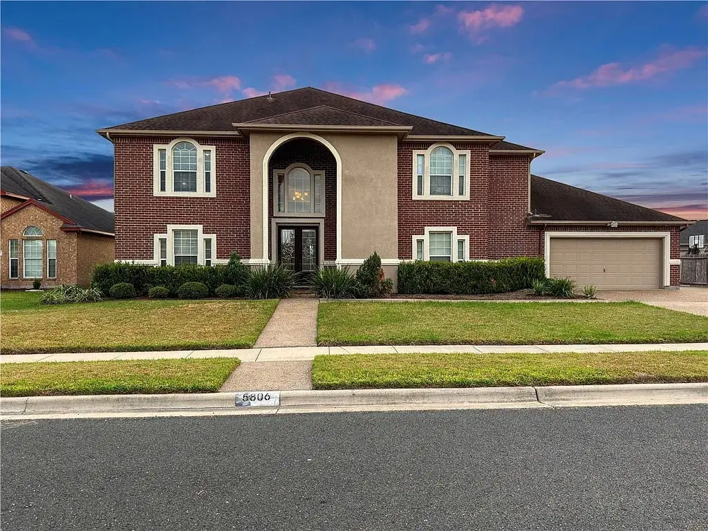Two-story brick house with a large driveway and well-maintained lawn at sunset.