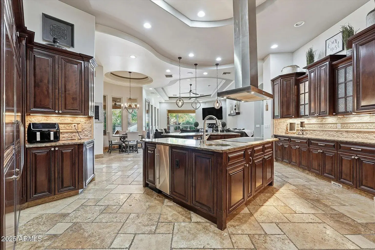 Spacious kitchen with dark wood cabinets, large island, and dining area in the background.