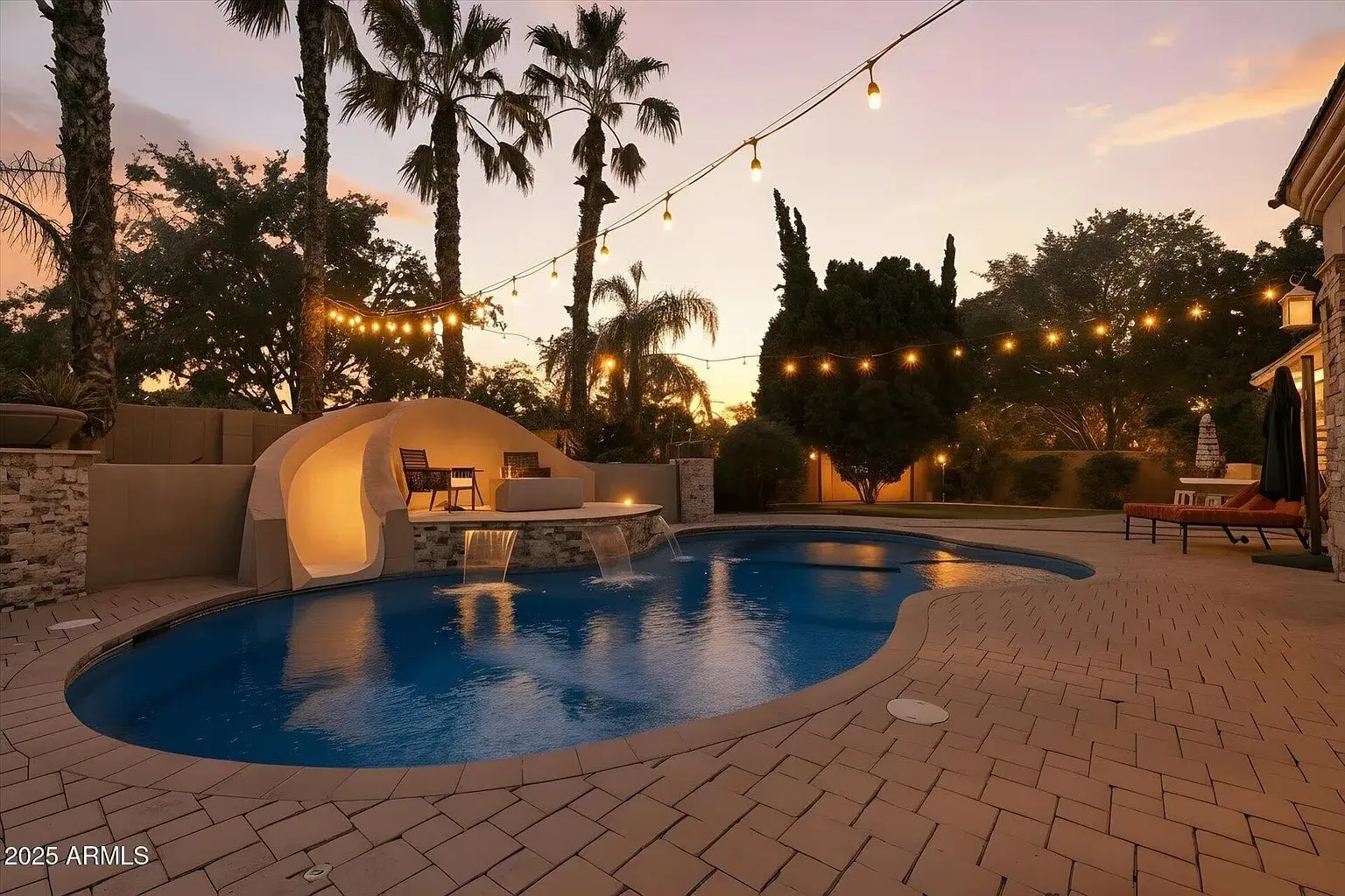 Backyard pool at sunset with string lights, palm trees, and a cozy seating area.