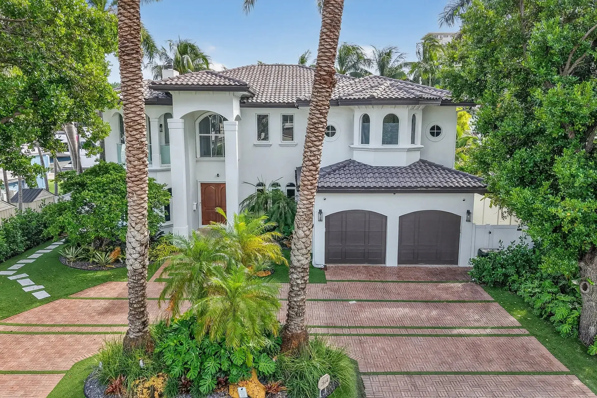 Large white two-story house with palm trees, a tiled roof, and a double garage.