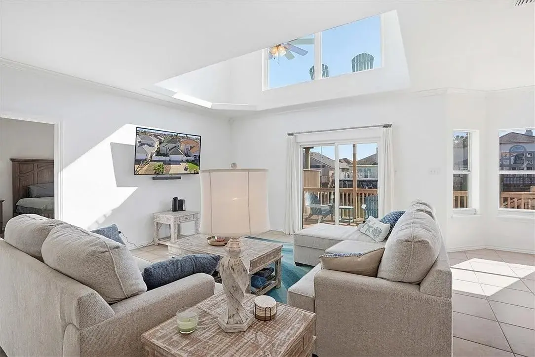Bright living room with beige sofas, TV, skylight, and access to a balcony.