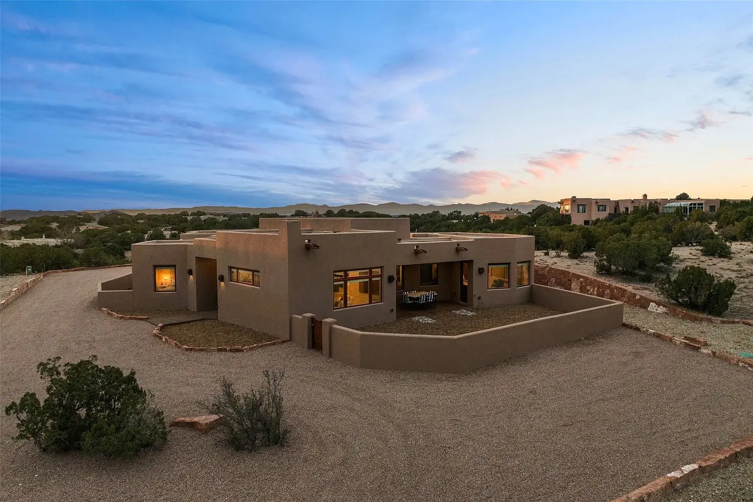 Modern adobe-style house in a desert landscape at sunset, with a gravel driveway.