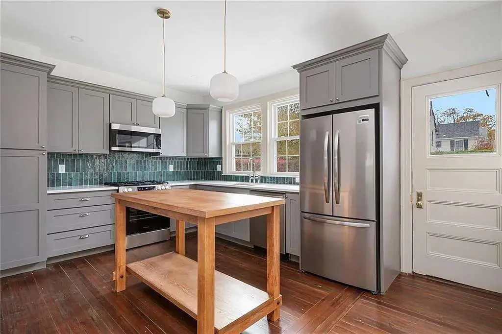 Modern kitchen with gray cabinets, stainless steel appliances, wooden island, and green tile backsplash.