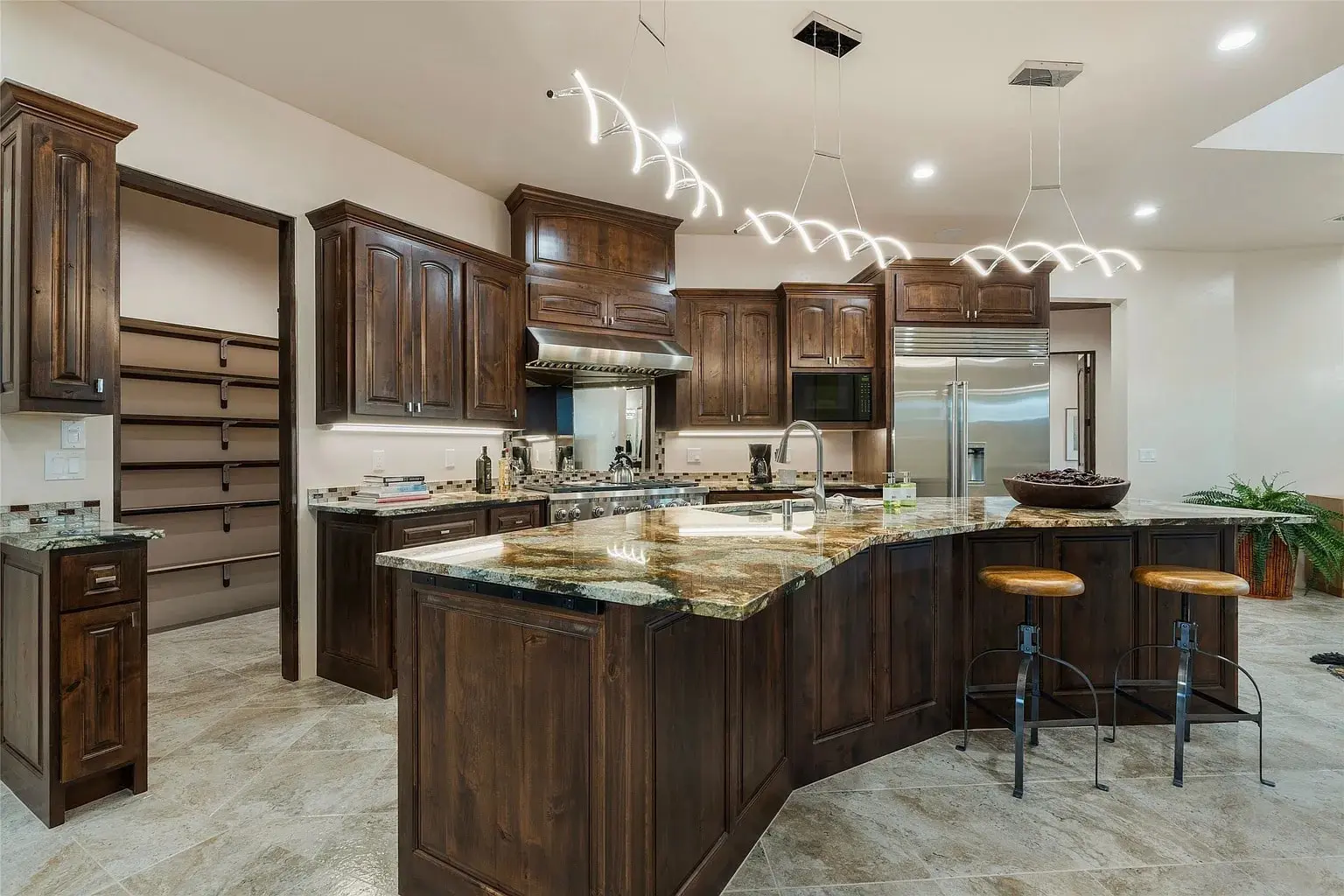 Modern kitchen with dark wood cabinets, marble countertops, island, bar stools, and unique pendant lighting.