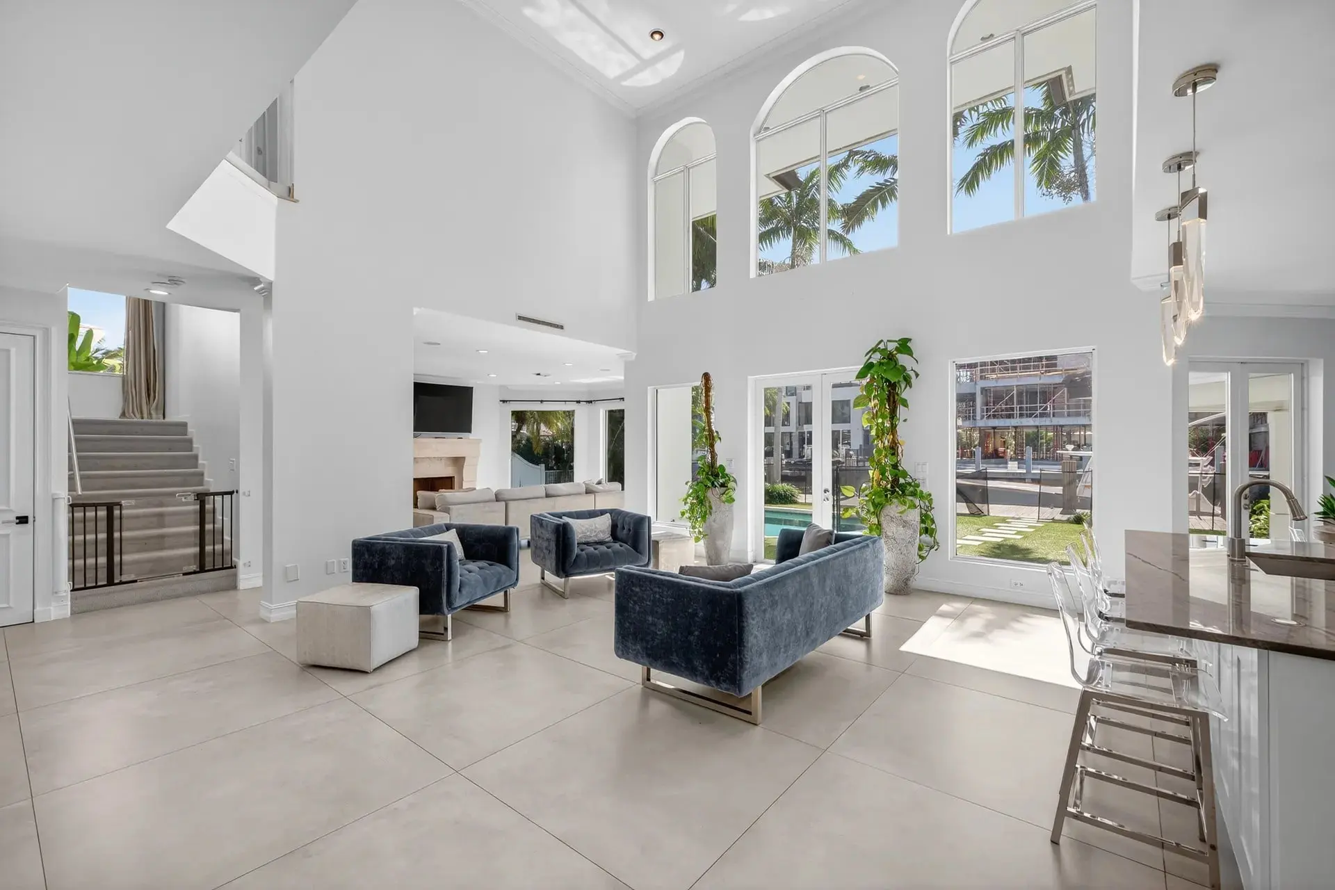 Spacious modern living room with high ceilings, large windows, blue sofas, and indoor plants.