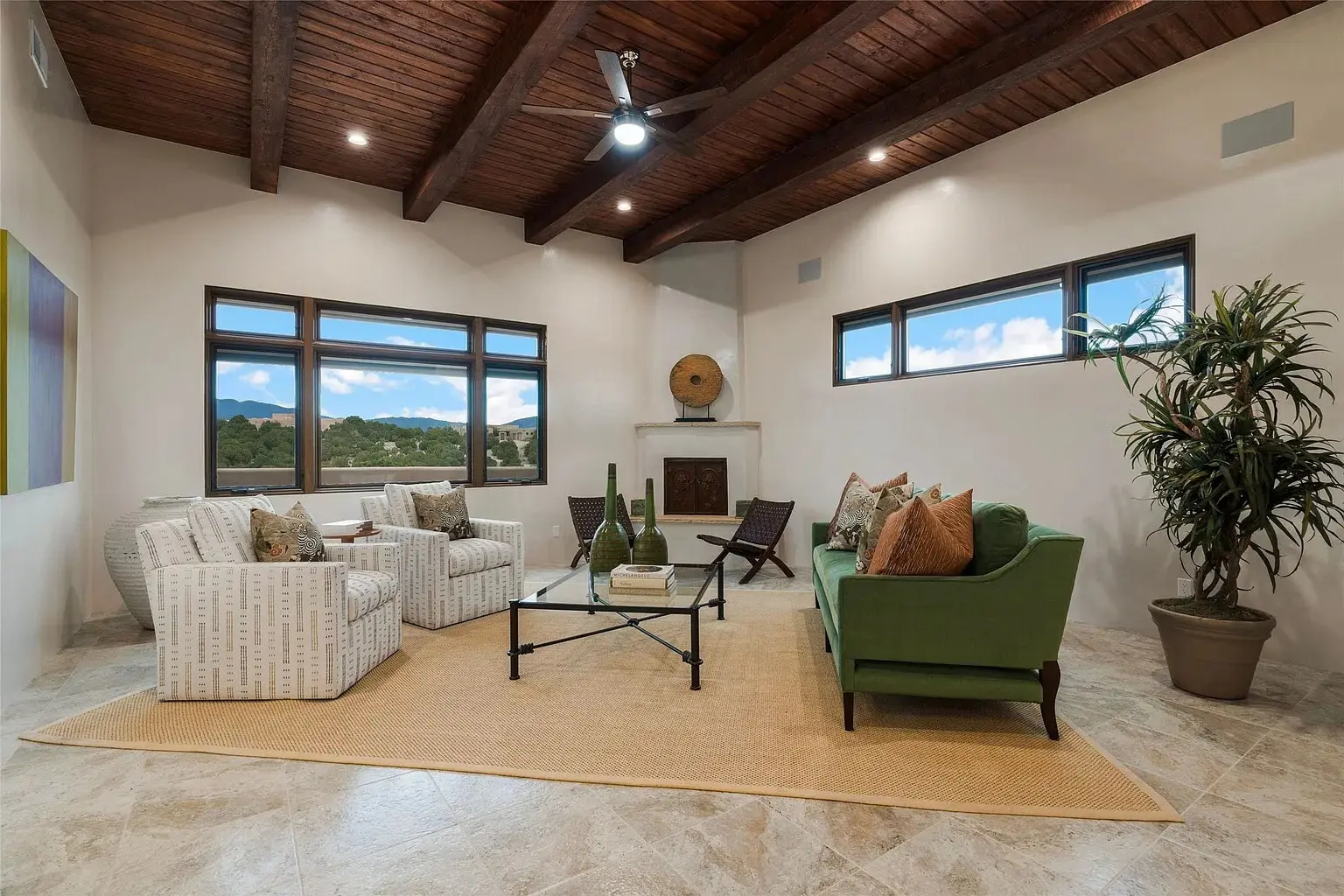 Modern living room with wooden ceiling, green sofa, armchairs, coffee table, and large windows with scenic view.