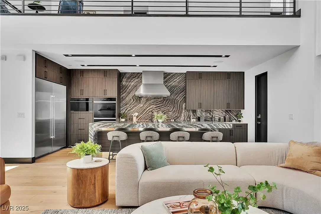 Modern kitchen and living area with wood cabinets, marble island, and beige sofa.