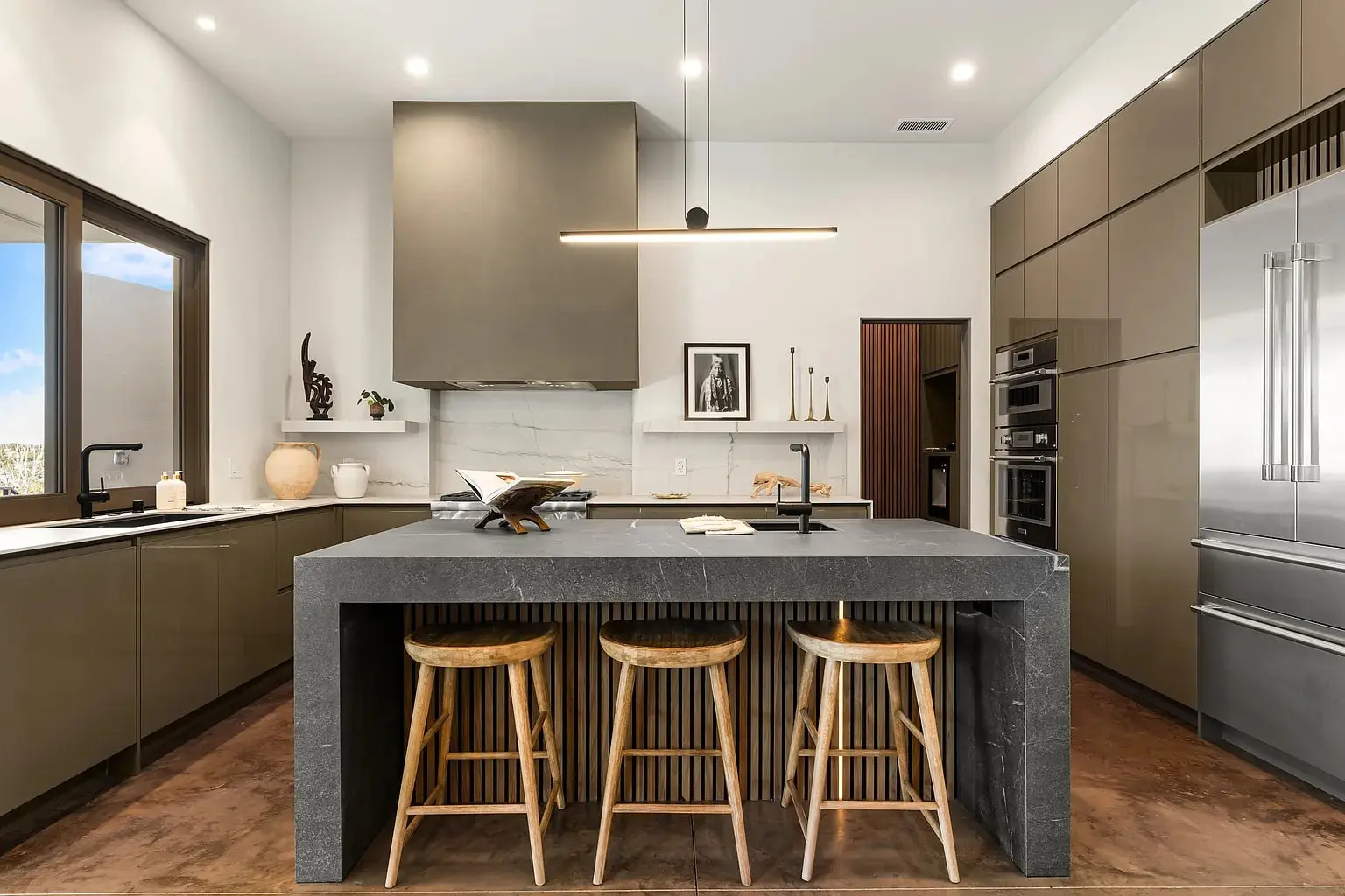 Modern kitchen with a large dark island, bar stools, and sleek cabinetry.