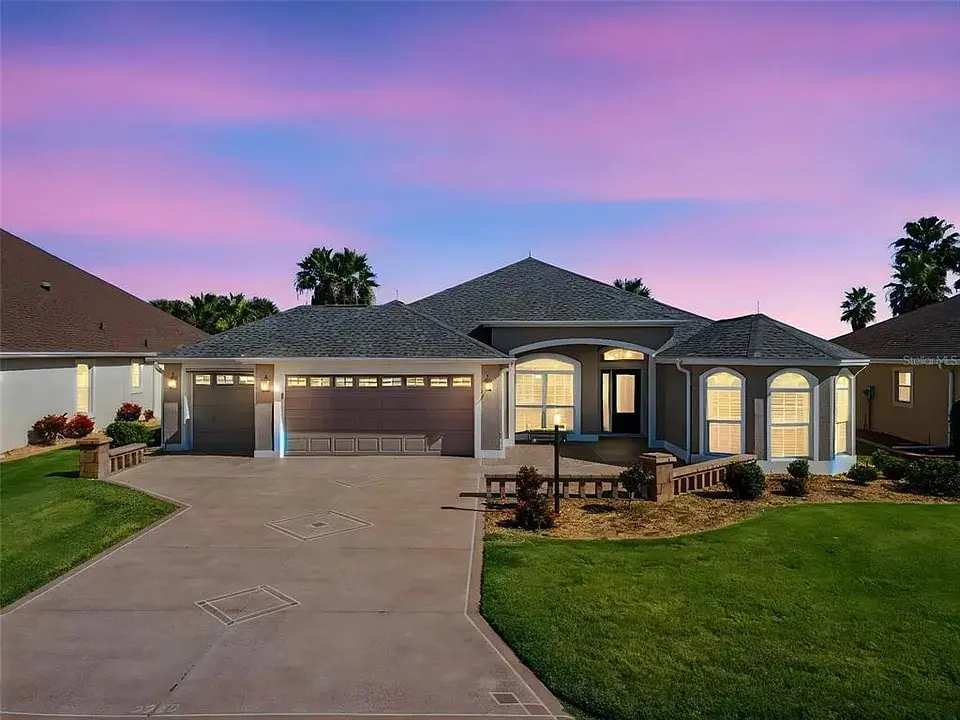 Single-story house with a three-car garage, lit at dusk under a pink and purple sky.