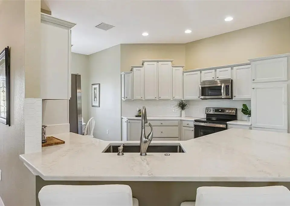 Modern kitchen with white cabinets, marble countertops, stainless steel appliances, and recessed lighting.