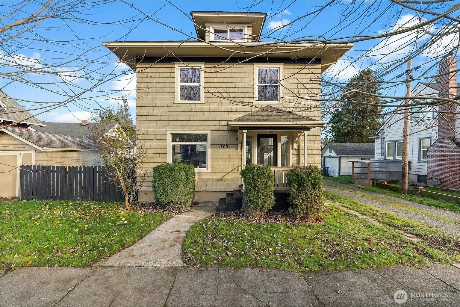 Two-story beige house with a small porch, surrounded by a lawn and bare trees.