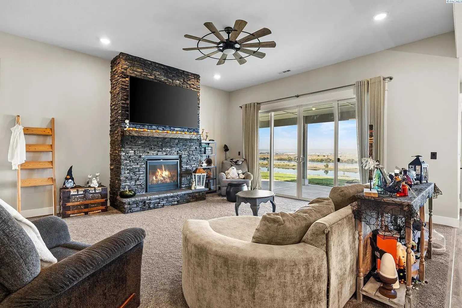 Spacious living room with stone fireplace, large TV, and sliding glass doors overlooking a scenic view.