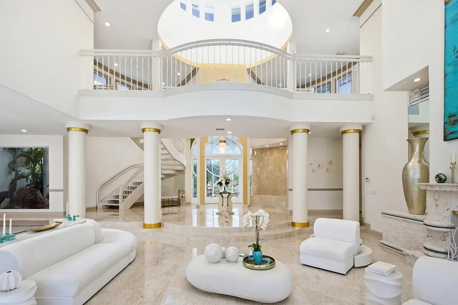 Spacious, elegant living room with white furniture, marble floors, and a grand staircase.