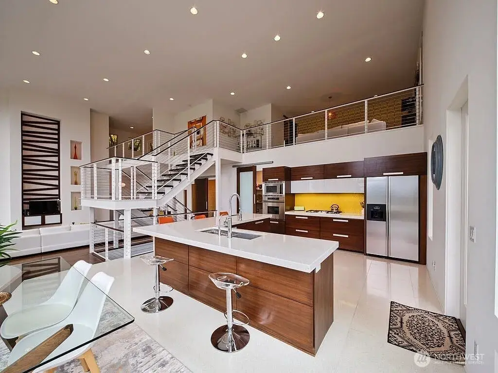 Modern open-plan kitchen and living area with a central island, staircase, and loft space.