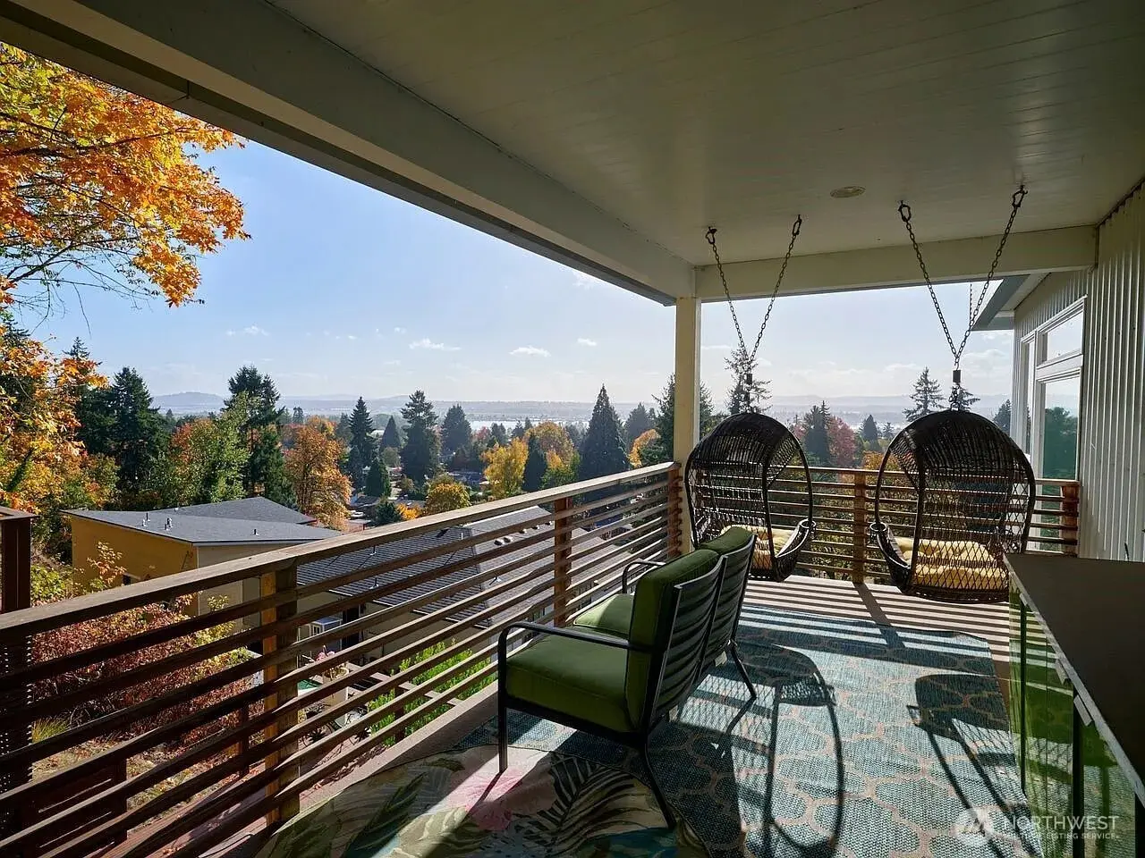 Covered balcony with hanging chairs and a view of trees and distant water under a clear sky.