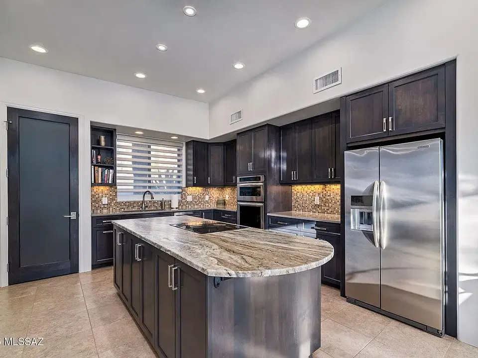 Modern kitchen with dark wood cabinets, stainless steel appliances, and a large marble island countertop.