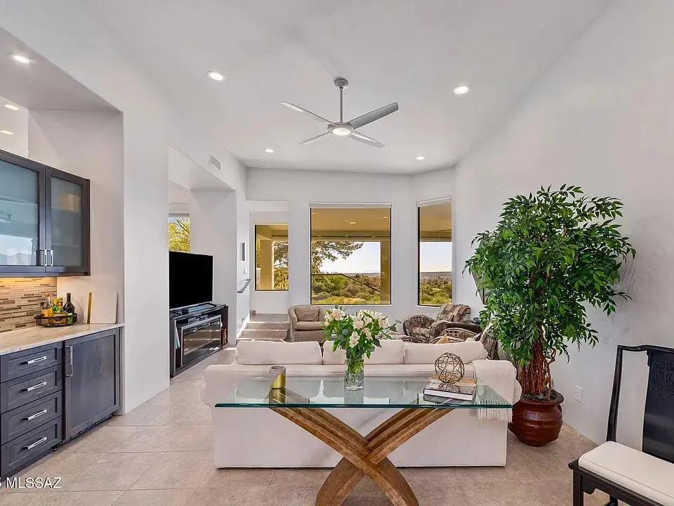 Modern living room with large windows, white sofa, glass table, and potted plant.