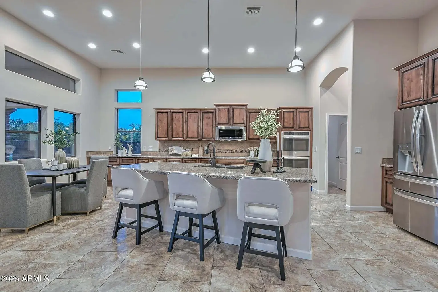 Modern kitchen with island, barstools, stainless steel appliances, and dining area with large windows.