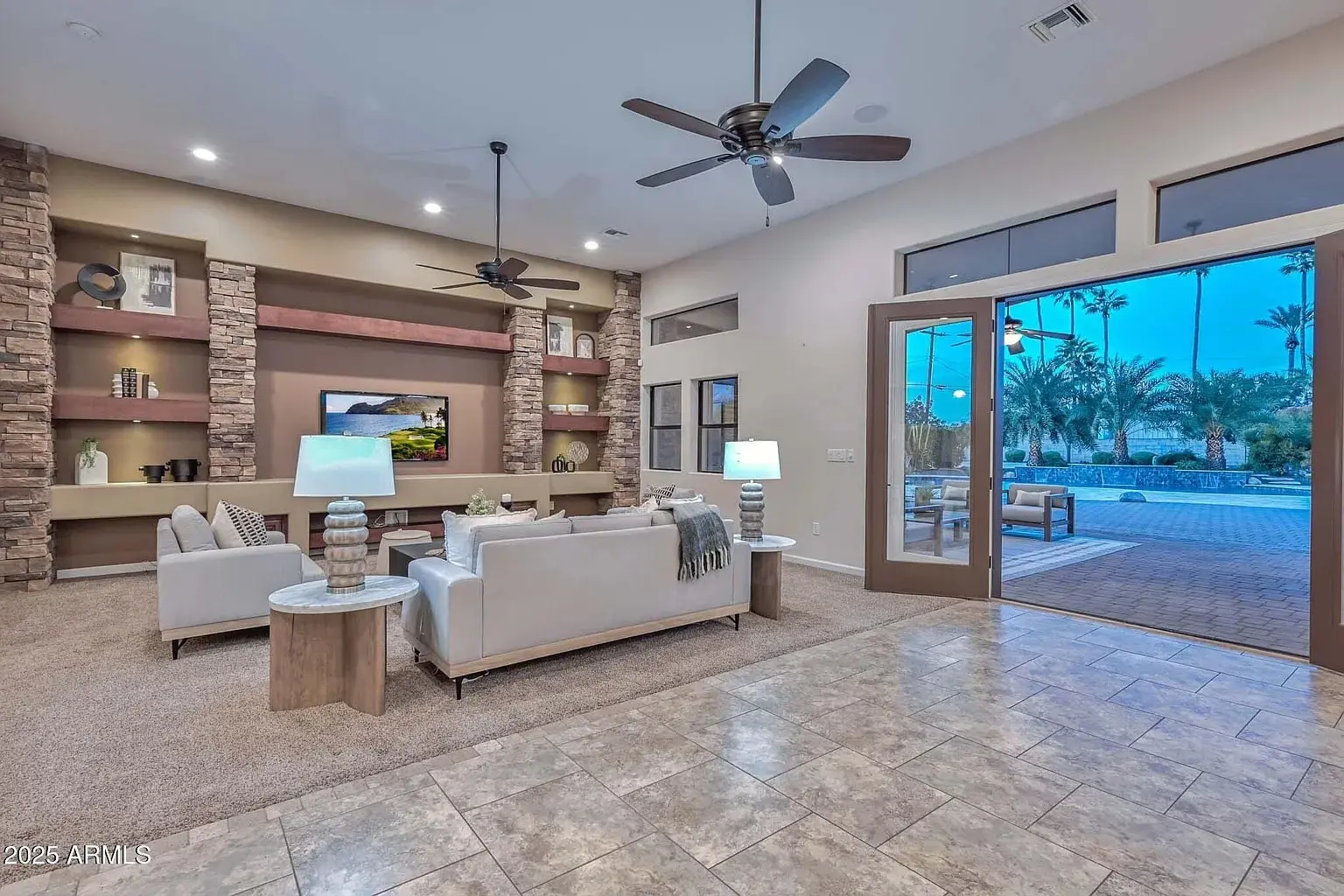 Spacious living room with modern decor, large windows, ceiling fans, and view of outdoor patio.