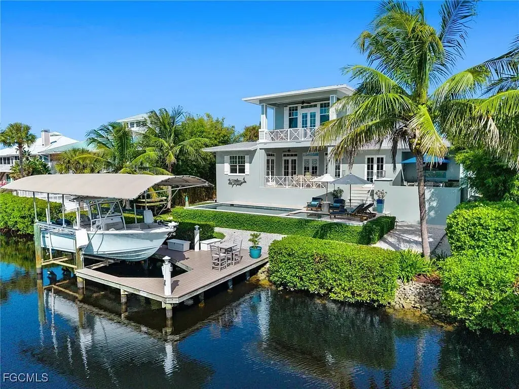 Waterfront house with a docked boat, surrounded by palm trees and lush greenery.