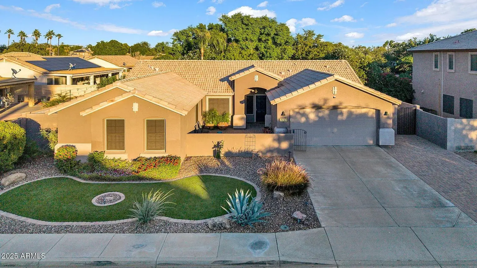 Single-story beige house with a two-car garage, desert landscaping, and a small front lawn.