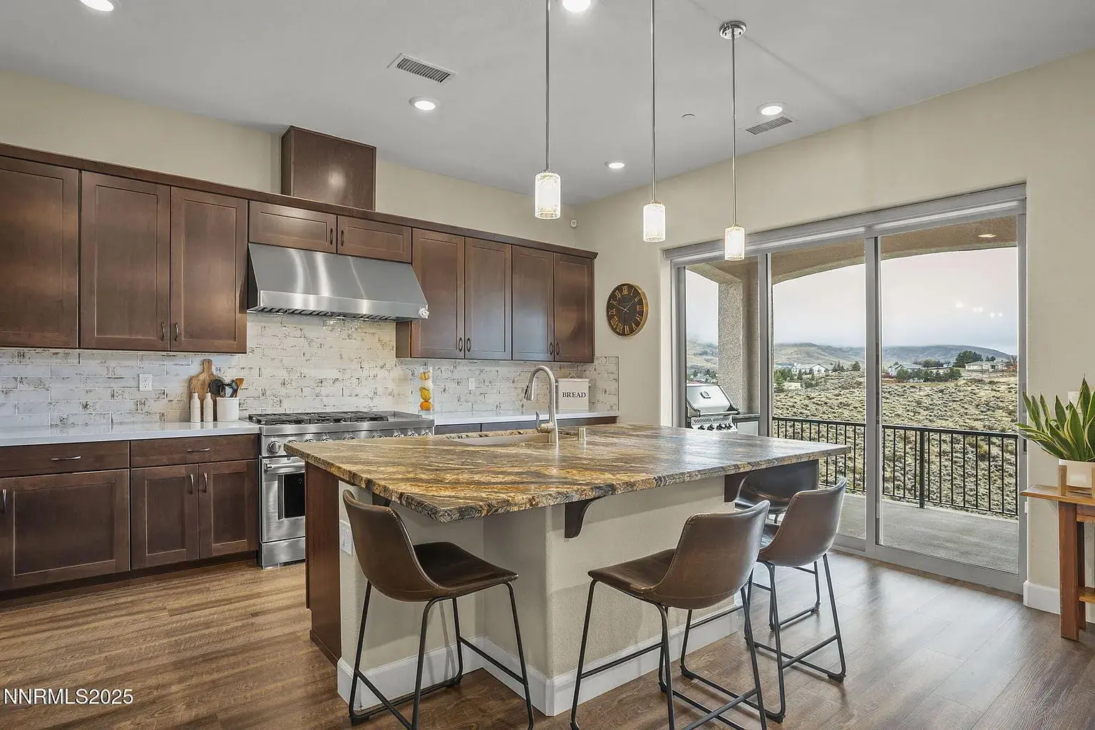 Modern kitchen with dark wood cabinets, marble island, pendant lights, and a view of a balcony.