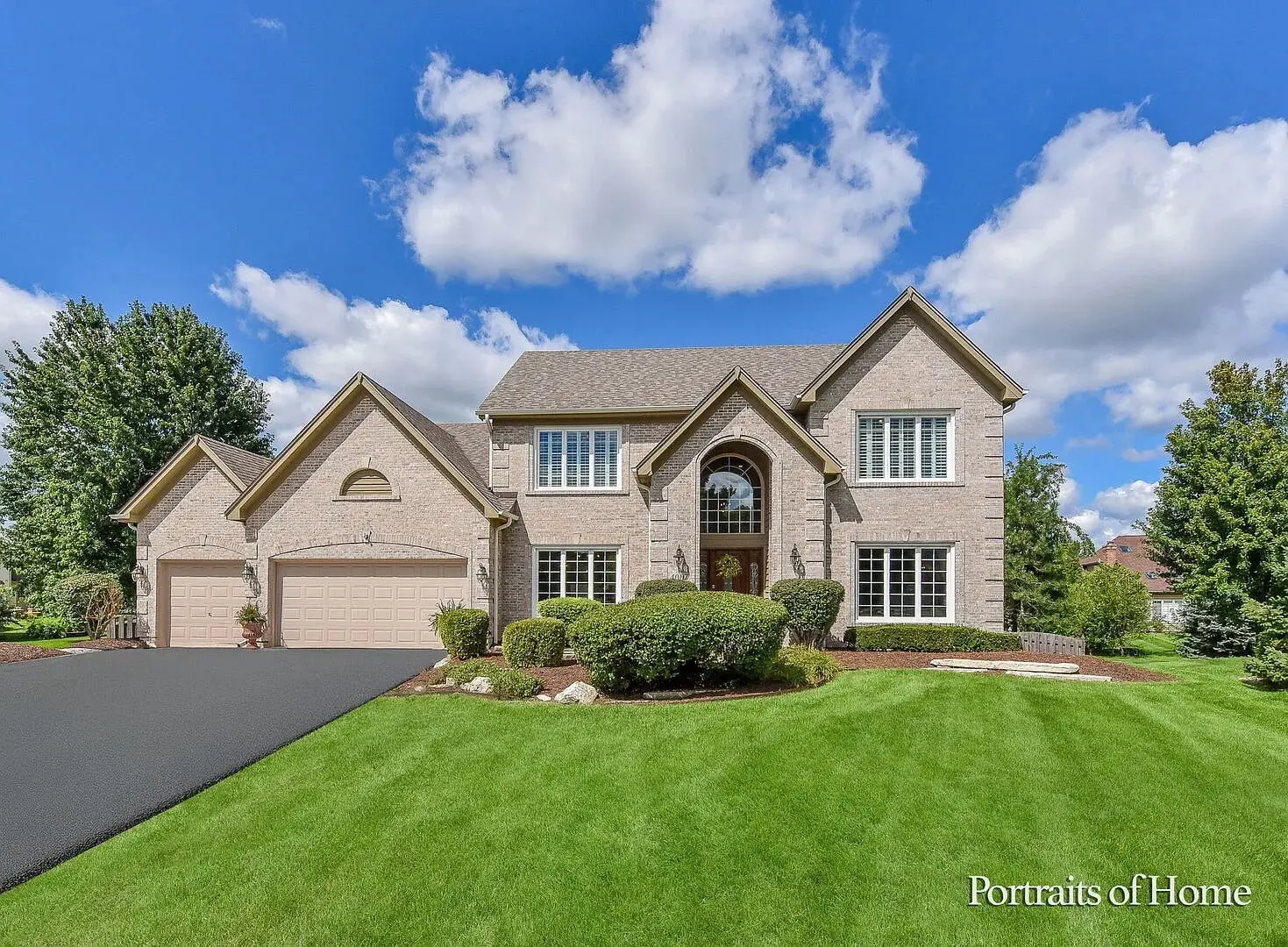 Large two-story brick house with manicured lawn and clear blue sky.