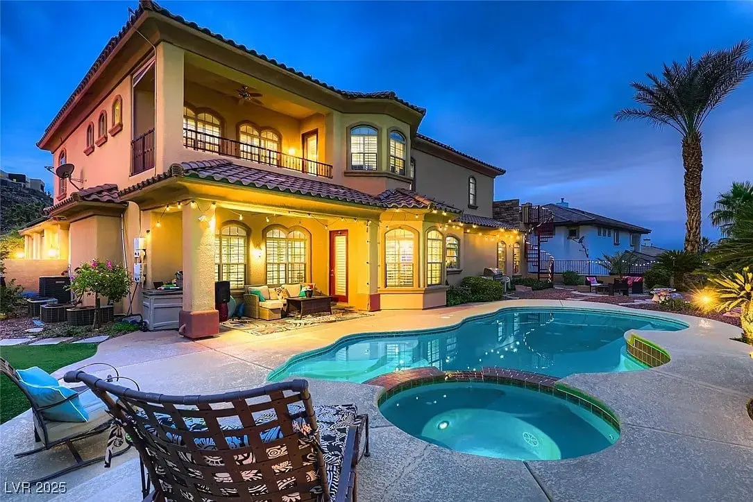Two-story house with a lit patio, pool, and spa in a landscaped backyard at dusk.