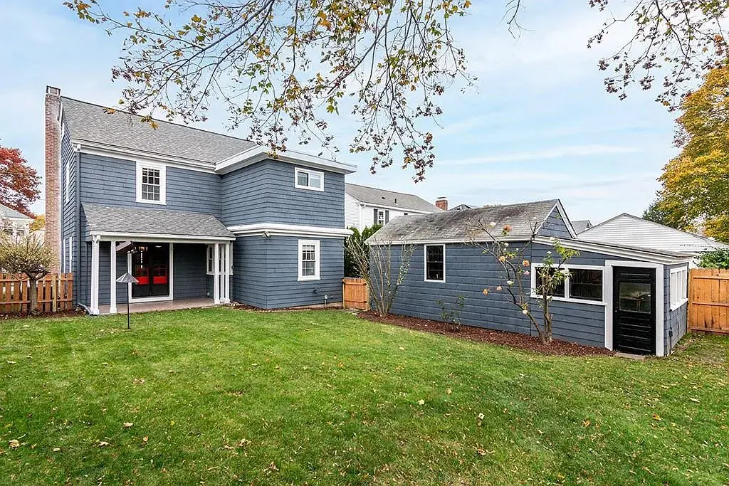 Blue two-story house with a porch, adjacent garage, and fenced backyard with grass and trees.