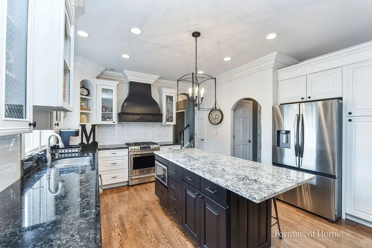 Modern kitchen with black and white cabinetry, stainless steel appliances, and a large granite island.