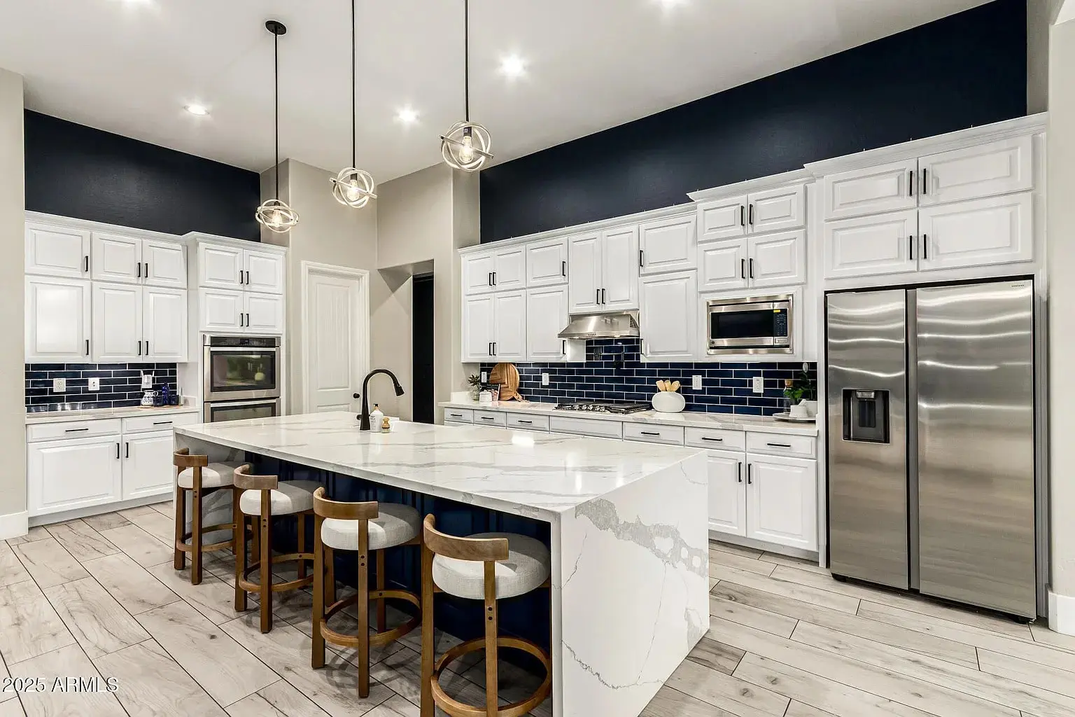 Modern kitchen with white cabinets, marble island, stainless steel appliances, and navy blue backsplash.